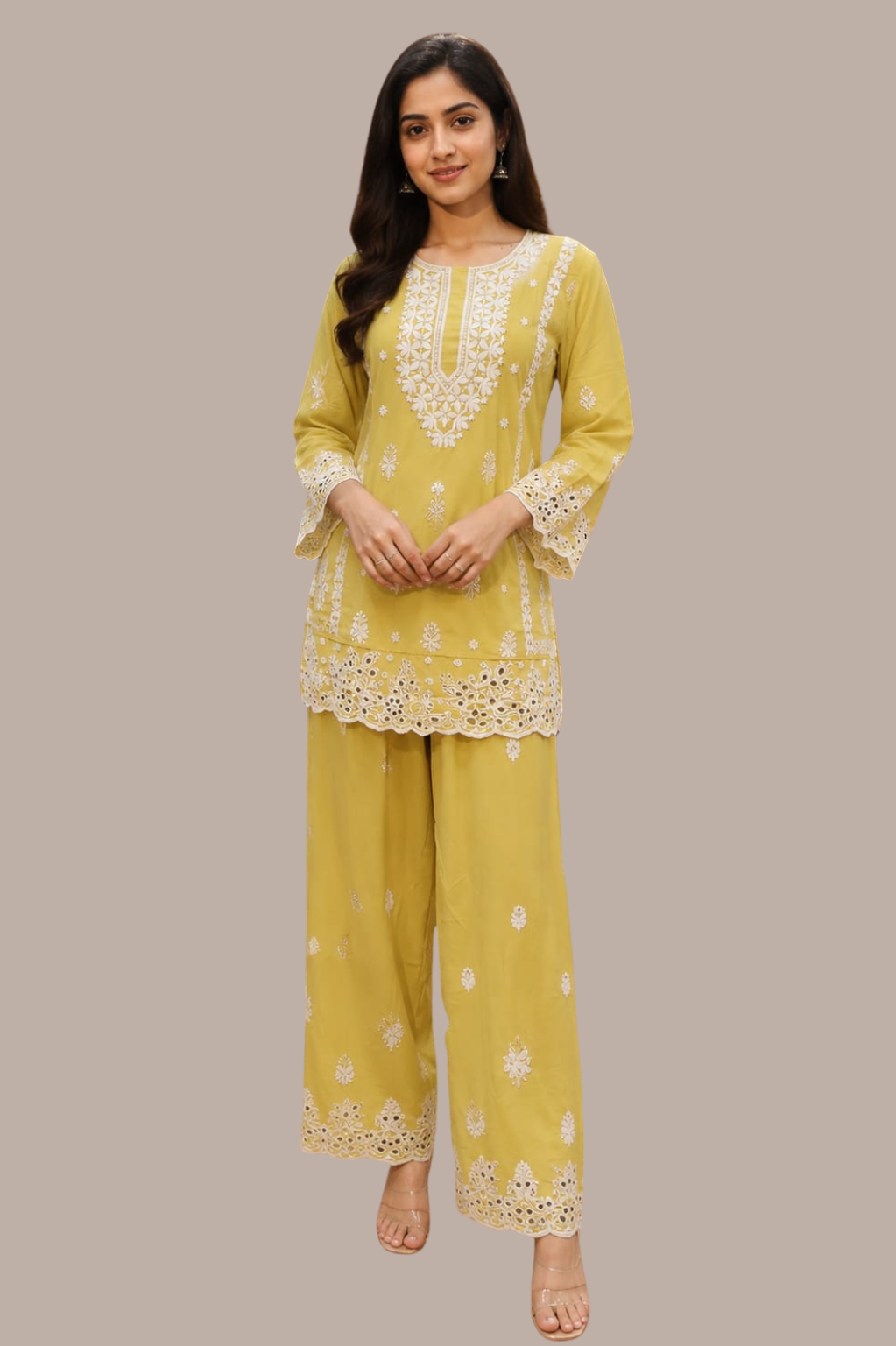 A woman modeling a yellow two-piece traditional outfit with white floral embroidery, featuring a long-sleeve kurta and matching wide-leg pants, set against a solid taupe background.