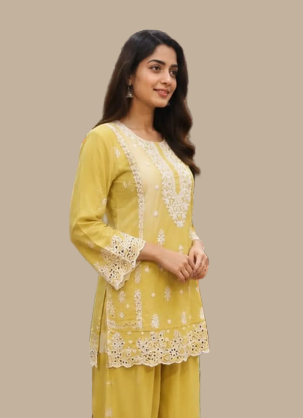 A woman modeling a yellow three-piece salwar kameez suit with white floral embroidery, standing inside a clothing store.