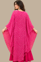 A woman seated in a yellow chair wearing a bright pink traditional outfit with a patterned embroidered bodice and a matching draped shawl, photographed in a retail store interior with shelves of folded garments in the background.