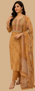 A woman modeling a traditional three-piece salwar kameez set in a fabric store. The set consists of a mustard yellow printed kameez kurta with floral embroidery on the neckline, matching trousers, and a sheer dupatta with a printed border.