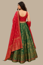 A woman modeling a traditional Indian lehenga choli dress from the back in a clothing store. The outfit features a green Banarasi silk skirt with intricate gold zari embroidery, a red embroidered blouse, and a red dupatta with gold borders.