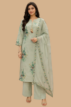A woman modeling a sage green ethnic salwar kameez suit with floral embroidery and a matching dupatta in a clothing store.
